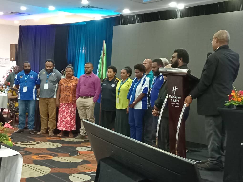 Delegates stand together at the 2025 National CHS General Assembly, demonstrating unity and collaboration. A speaker addresse