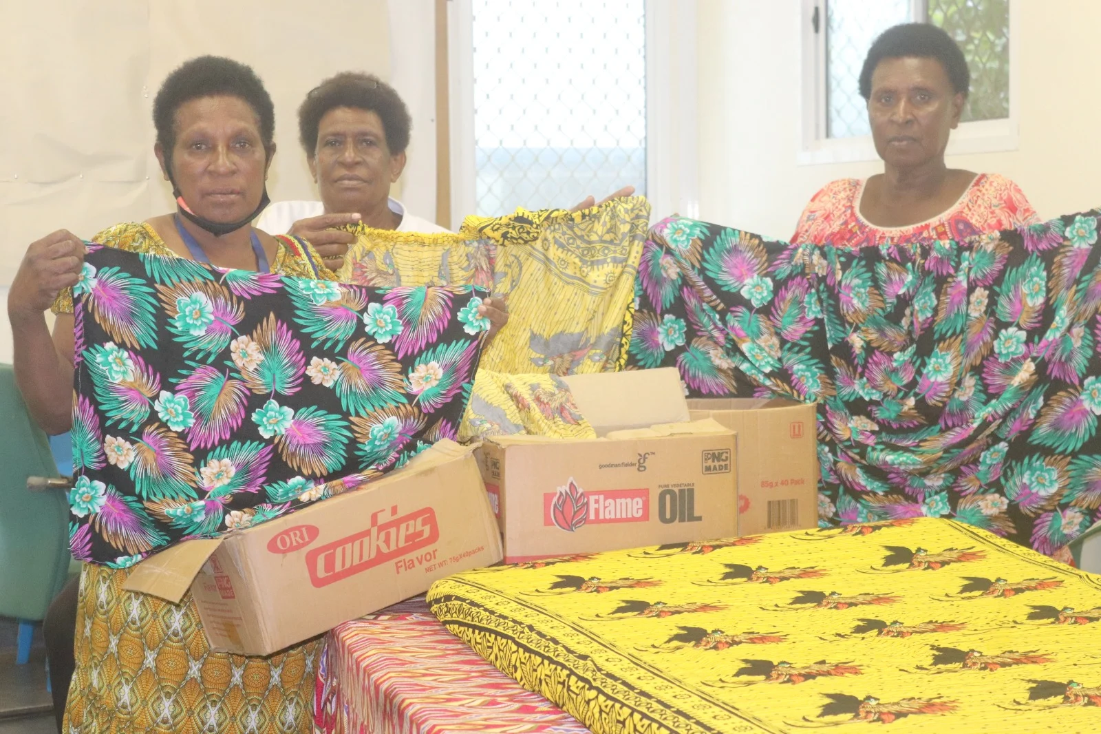 Three women proudly display colorful fabric pieces during a Women’s Day celebration with ECPNG Health Services, highlighting