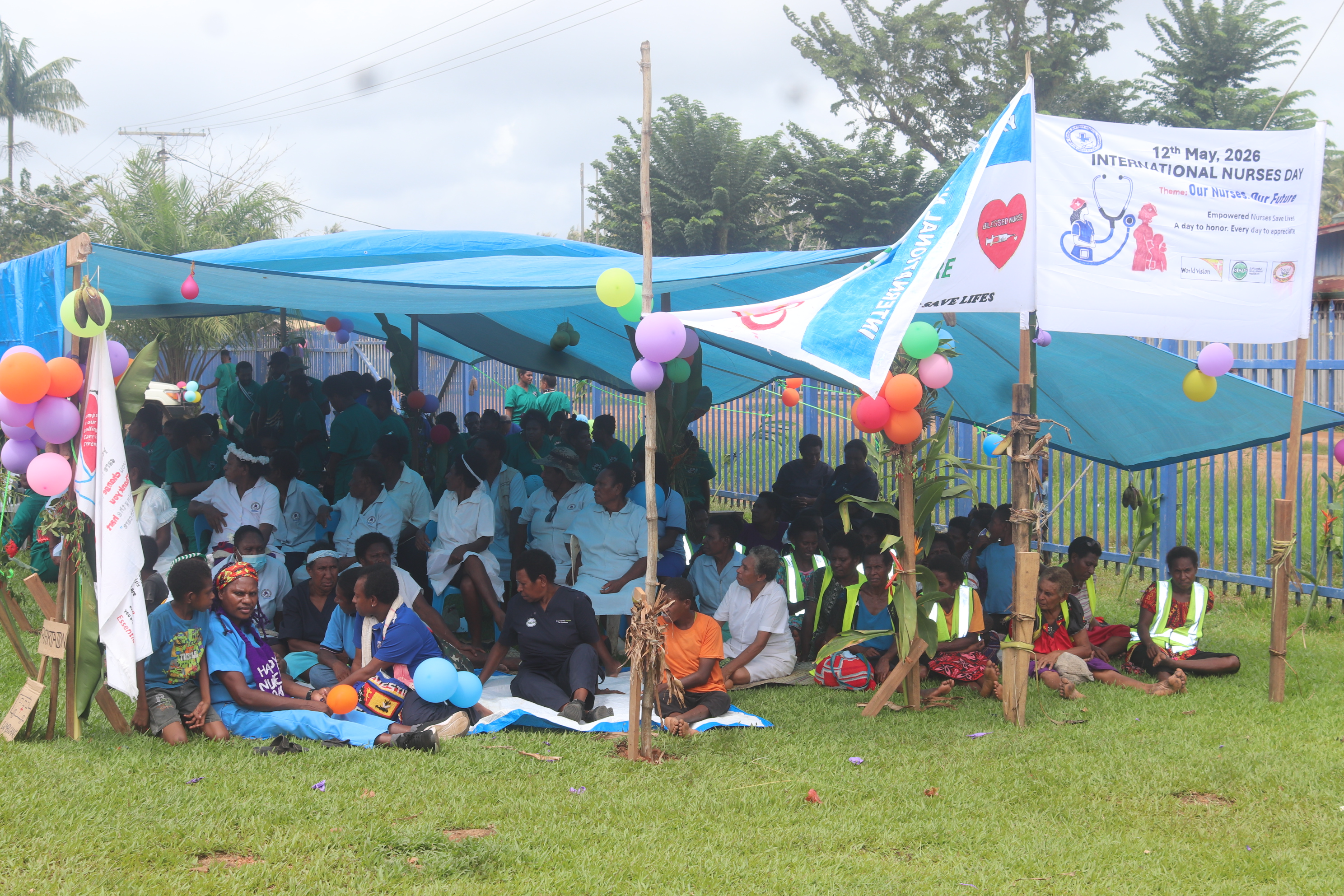 Staff, partners, and community members gather under decorated canopies at Balimo District Hospital to celebrate International